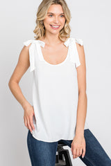 woman wearing a white tank top with tie shoulder details and blue jeans