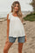 woman wearing a white maternity top with bow details and denim shorts, showing off her baby bump on the beach