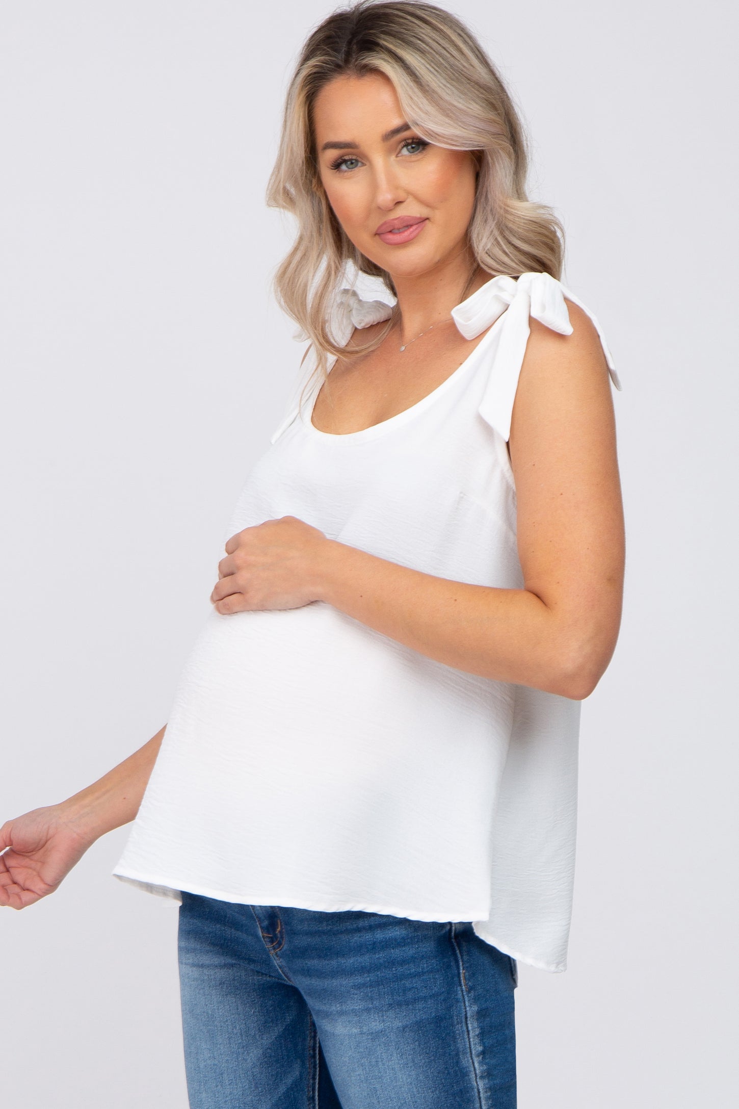 woman wearing a white maternity top with tie straps and a visible baby bump, paired with jeans
