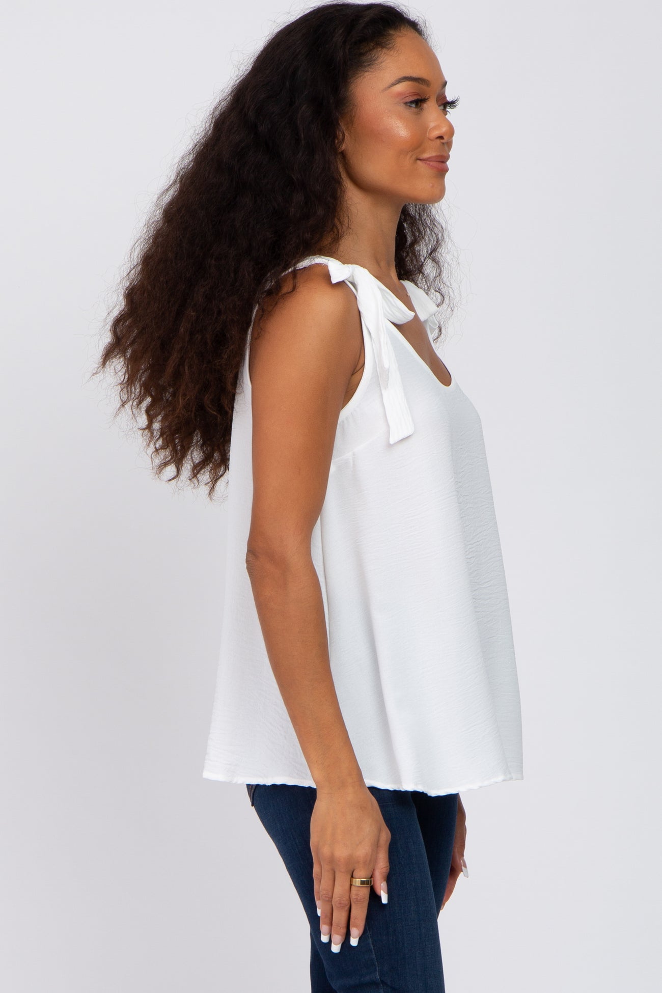 woman wearing a white sleeveless top with tie shoulder details and blue denim jeans