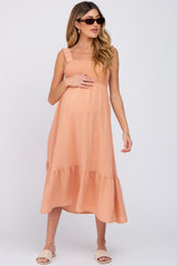 woman wearing a peach maternity dress with a smocked bodice and ruffled straps, holding her baby bump