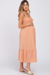 woman wearing a peach maternity dress with ruffled straps and a flowy skirt, showing her baby bump