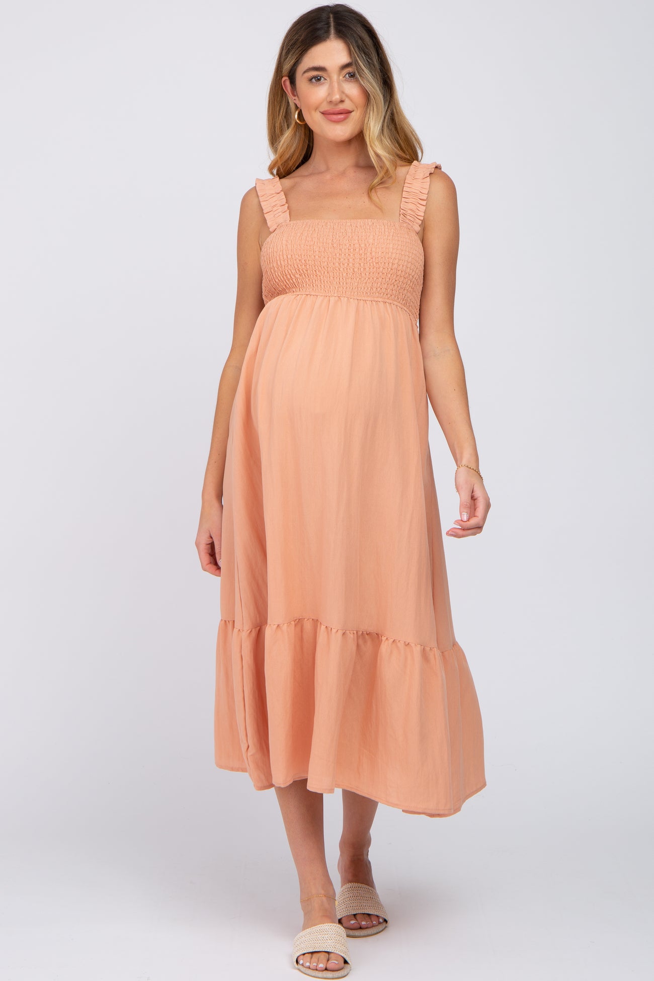 woman wearing a peach maternity dress with frill straps and a flowing skirt, showcasing her baby bump