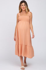 woman wearing a peach maternity dress with frill straps and a flowing skirt, showcasing her baby bump