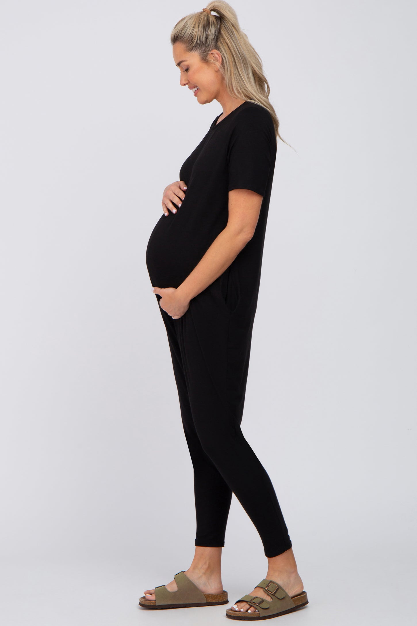 woman wearing a black short sleeve maternity jumpsuit and showing her baby bump