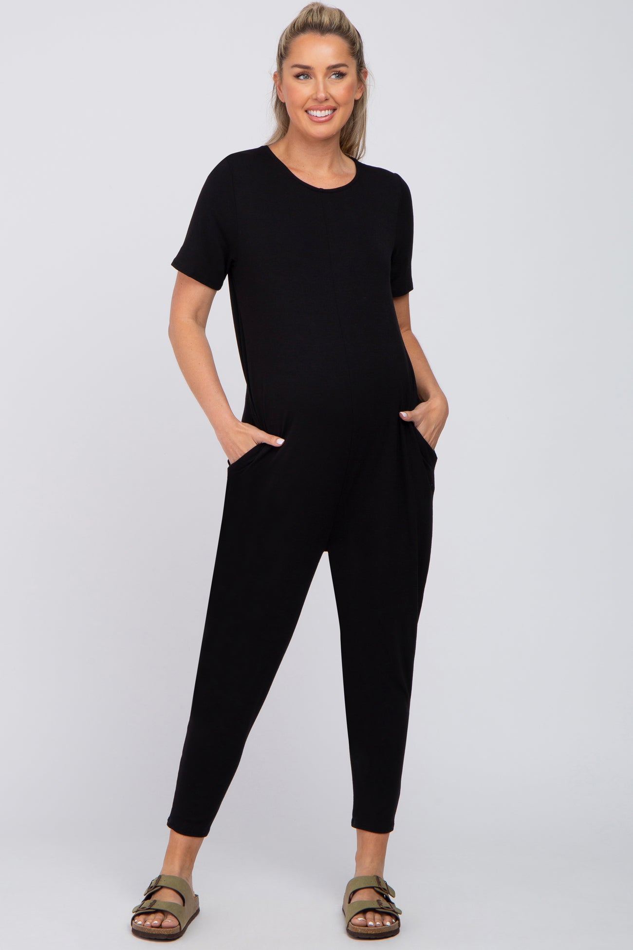 pregnant woman wearing a black short sleeve maternity jumpsuit with pockets and olive green sandals