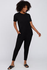woman wearing a black short sleeve jumpsuit with side pockets and a relaxed fit, posing confidently