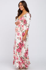 woman wearing a white floral print maternity maxi dress and holding her baby bump