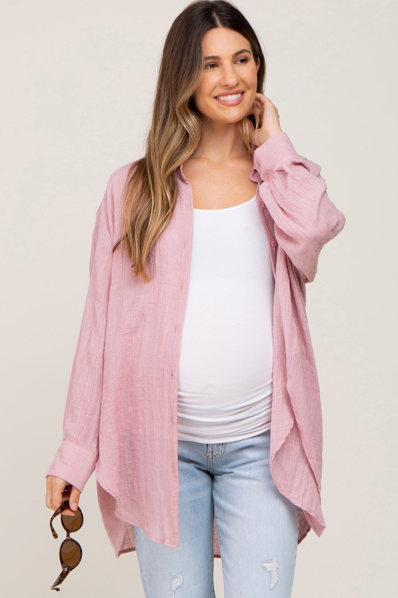 woman wearing a light pink maternity button-up shirt over a white tank top and blue jeans, showing a baby bump