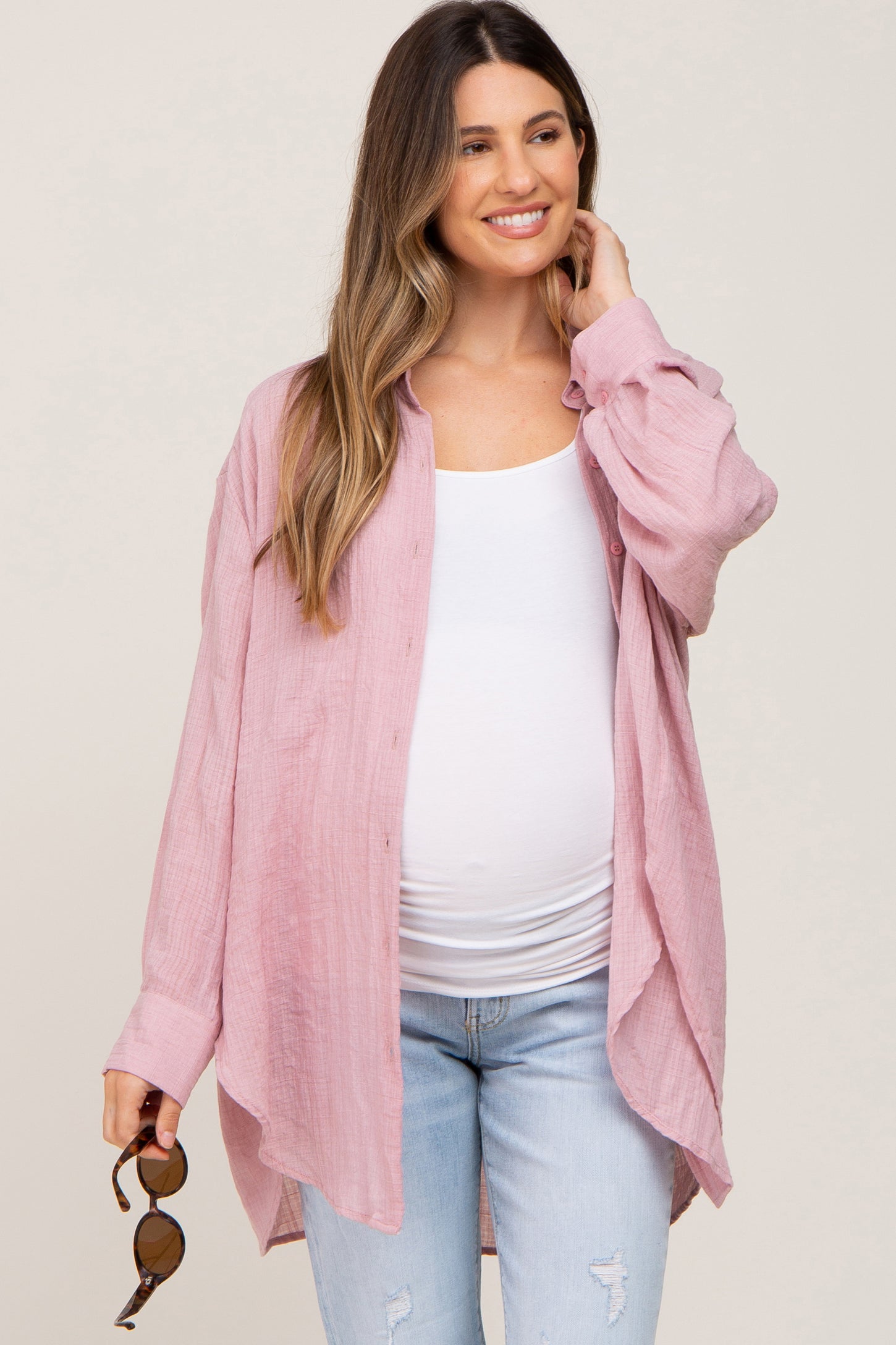 woman wearing a light pink maternity button-up shirt over a white tank top and blue jeans, showing a baby bump