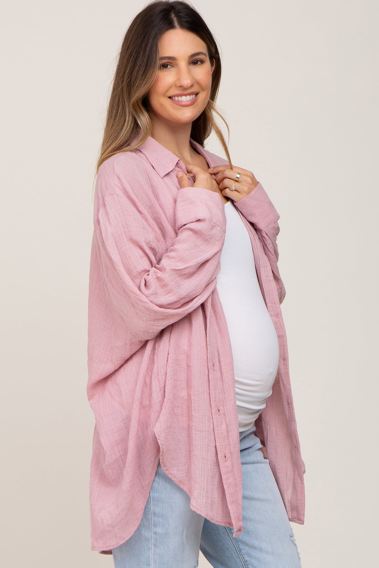 woman wearing a light pink maternity button-up shirt with a relaxed fit, showing her baby bump and paired with light blue jeans