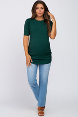 woman wearing a dark green maternity top with short sleeves and ruched sides, paired with light blue jeans