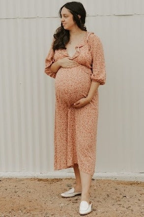 woman wearing a floral maternity dress with ruffles, cradling her visible baby bump