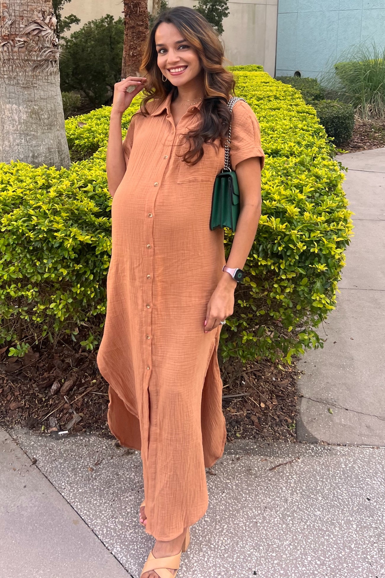 woman wearing a rust-colored button-up maternity dress with short sleeves and a visible baby bump