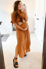 woman wearing a rust-colored short sleeve maternity dress with a belted waist and holding her baby bump in front of a mirror