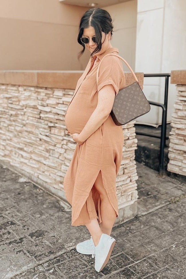 woman wearing a rust-colored short sleeve maternity dress highlighting her baby bump, paired with white sneakers and a brown handbag