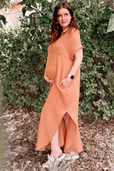 woman wearing an orange maternity maxi dress with short sleeves and pockets, cradling her baby bump outdoors