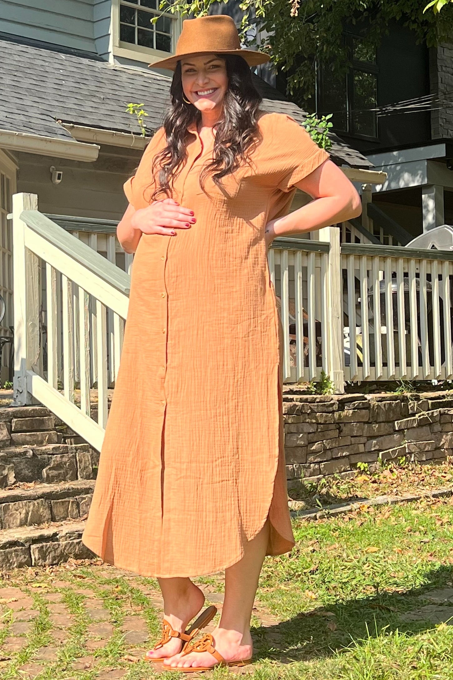 woman wearing a rust-colored maternity dress with buttons and holding her baby bump outdoors