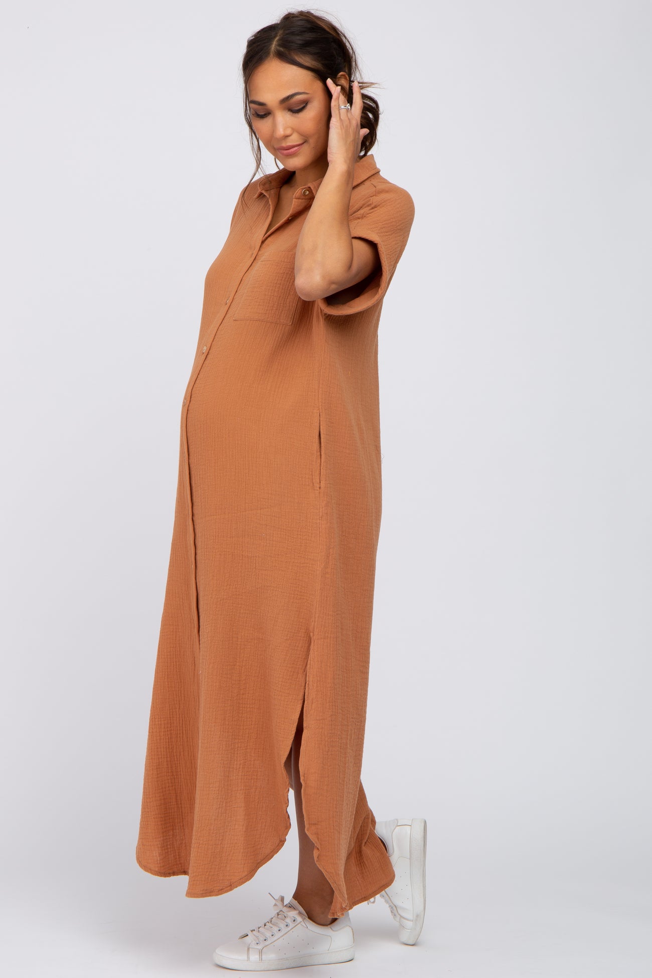 Pregnant woman wearing a short sleeve camel gauze maternity maxi shirt dress and white sneakers
