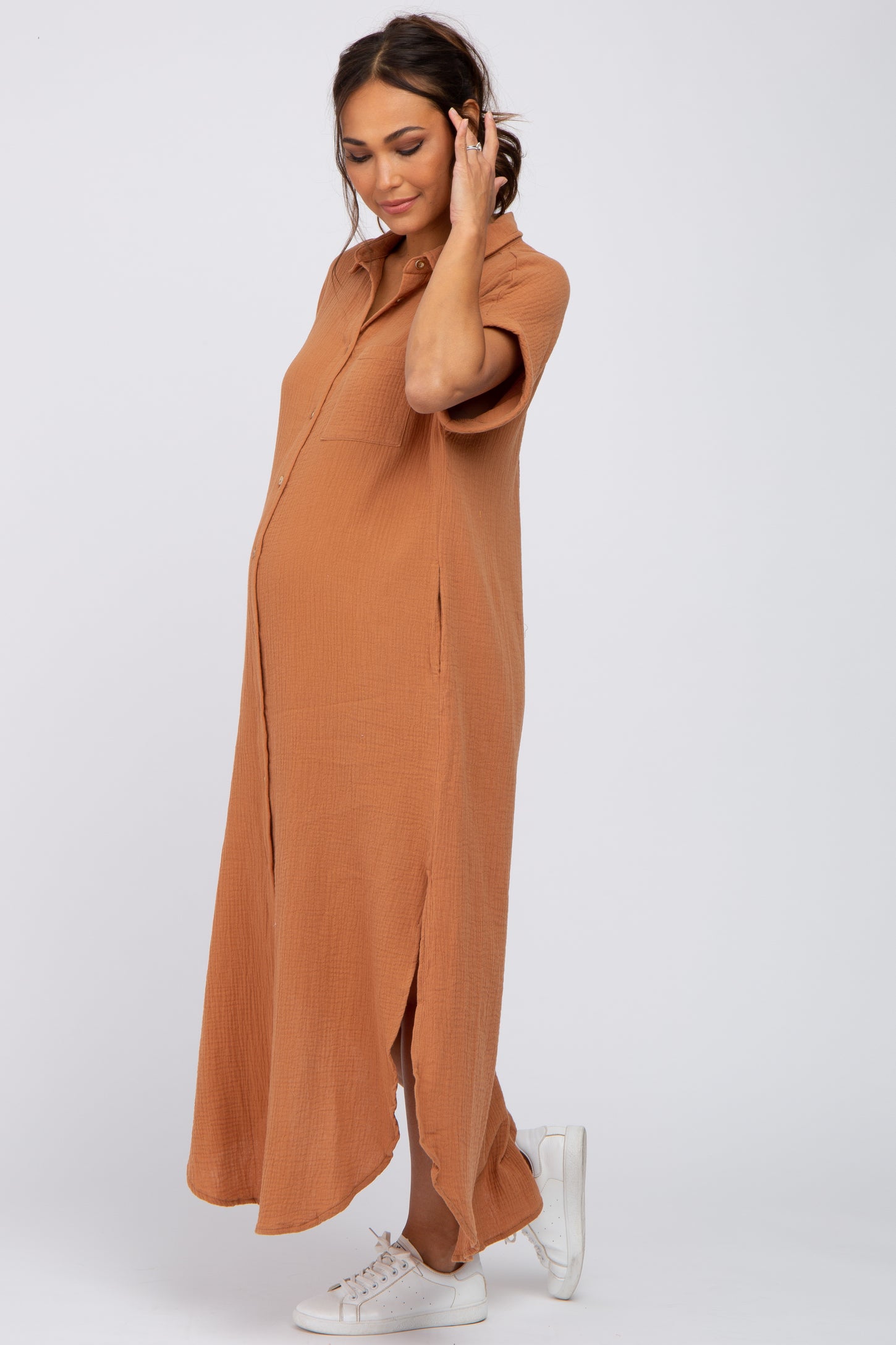Pregnant woman wearing a short sleeve camel gauze maternity maxi shirt dress and white sneakers