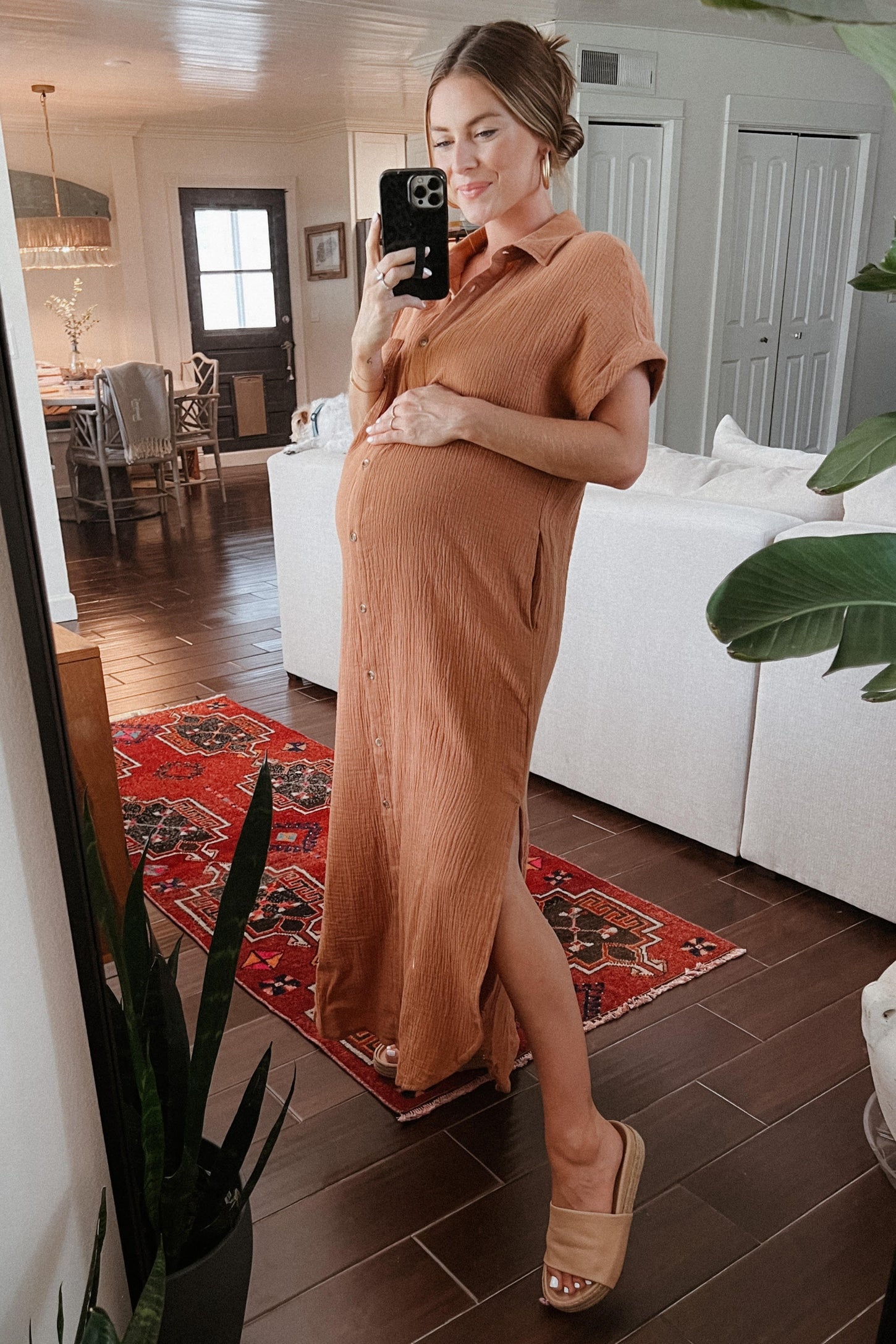 woman wearing a rust-colored maternity dress with buttons, showing her baby bump while standing in a living room