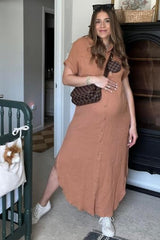 Pregnant woman in a tan button-down maxi dress and white sneakers posing in a nursery with a crossbody bag.
