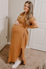 woman wearing a rust-colored linen maternity maxi dress with side slits and a visible baby bump