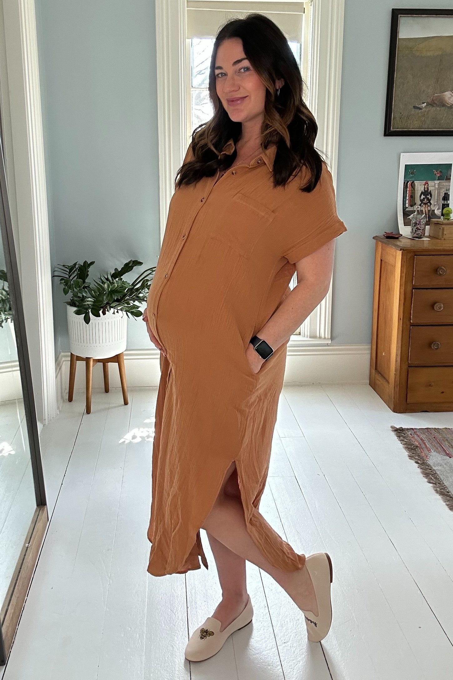 woman wearing a rust-colored maternity shirt dress with a side slit, showcasing her baby bump while posing indoors