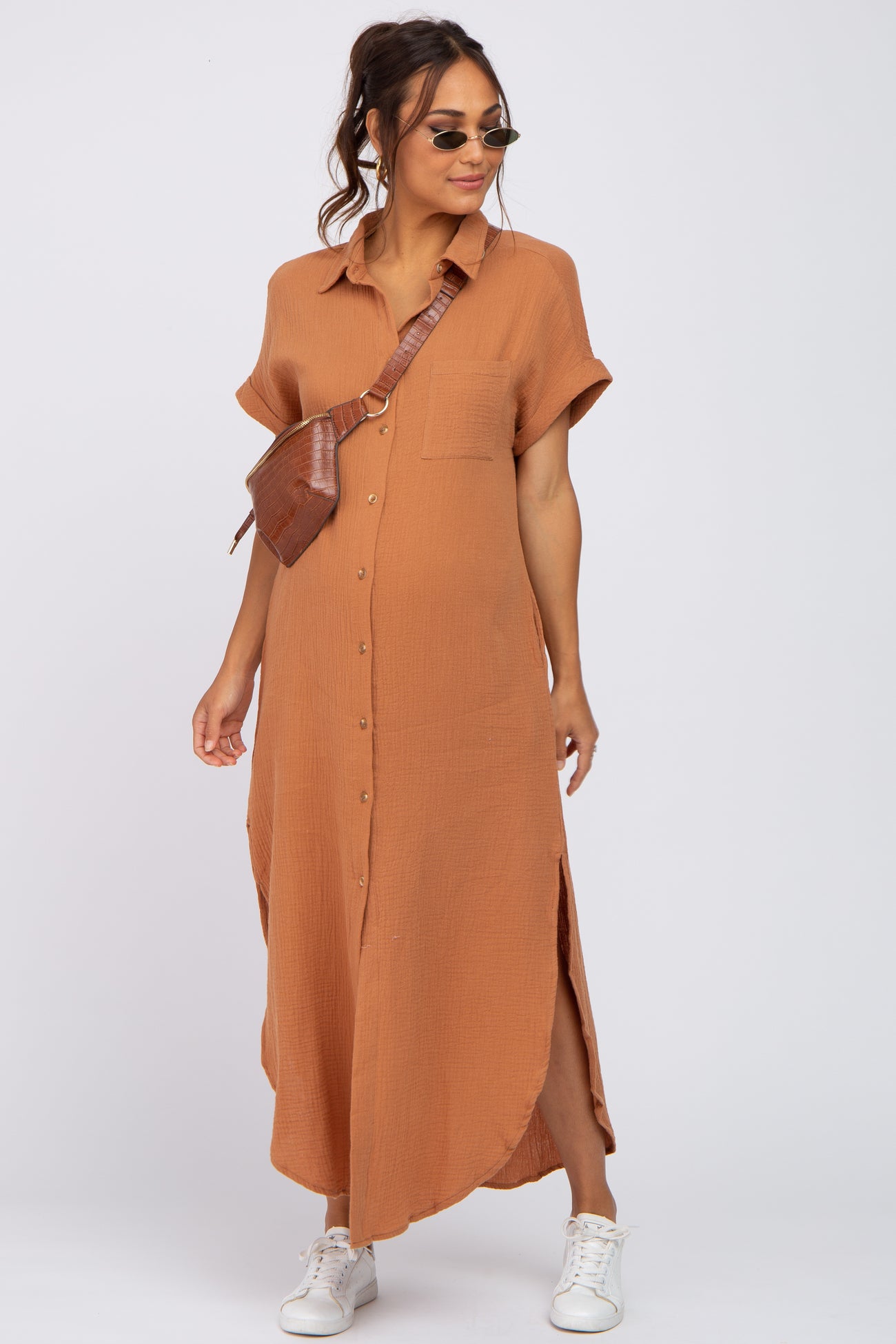 woman wearing a rust-colored maternity button-up dress with short sleeves and side slits, accessorized with a brown crossbody bag