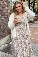 woman wearing a floral maxi dress with a cream cardigan, holding a drink while outdoors