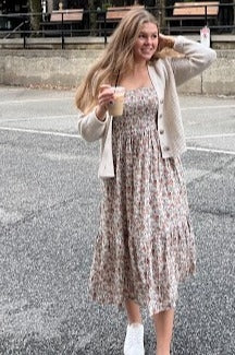 woman wearing a floral print midi dress and a light beige cardigan, holding an iced coffee and smiling