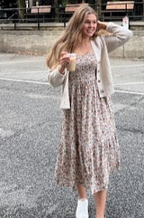 woman wearing a floral print midi dress and a light beige cardigan, holding an iced coffee and smiling