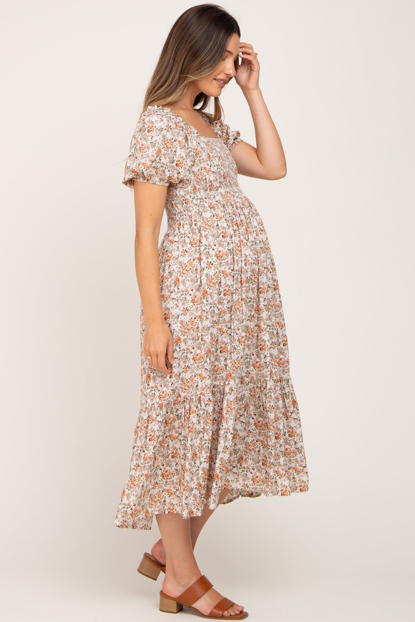 woman wearing a floral print maternity dress with short puff sleeves and a flowing skirt, gently touching her baby bump