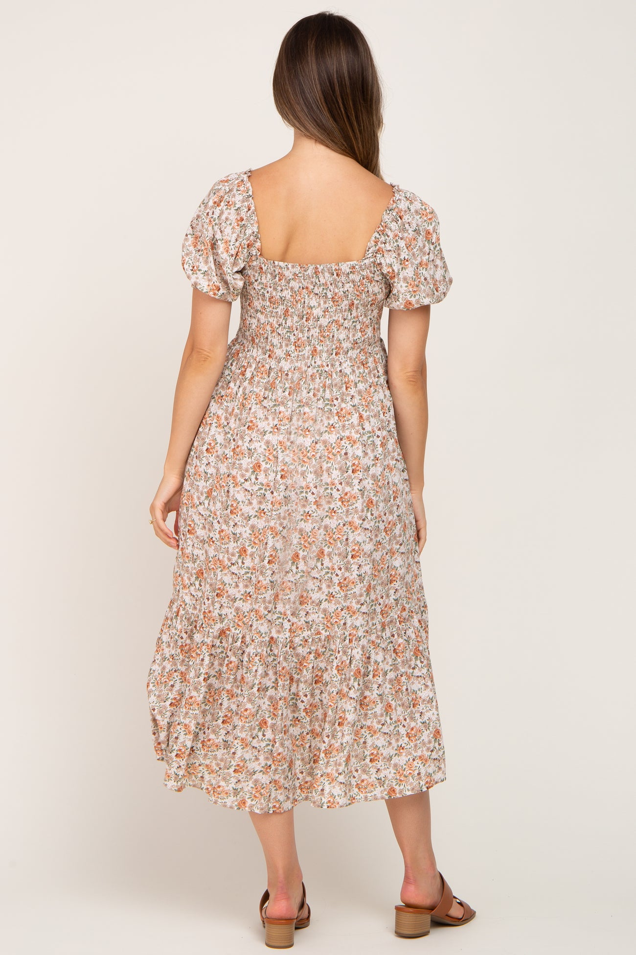 woman wearing a floral print maternity dress with puff sleeves and a tiered hemline, showing a baby bump from the back