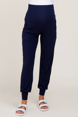 Woman wearing navy blue maternity joggers with a high waistband and white slide sandals