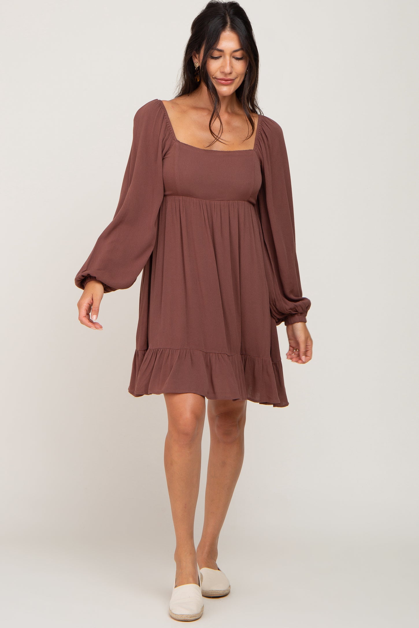 woman wearing a brown long sleeve mini dress with a square neckline and ruffle hem