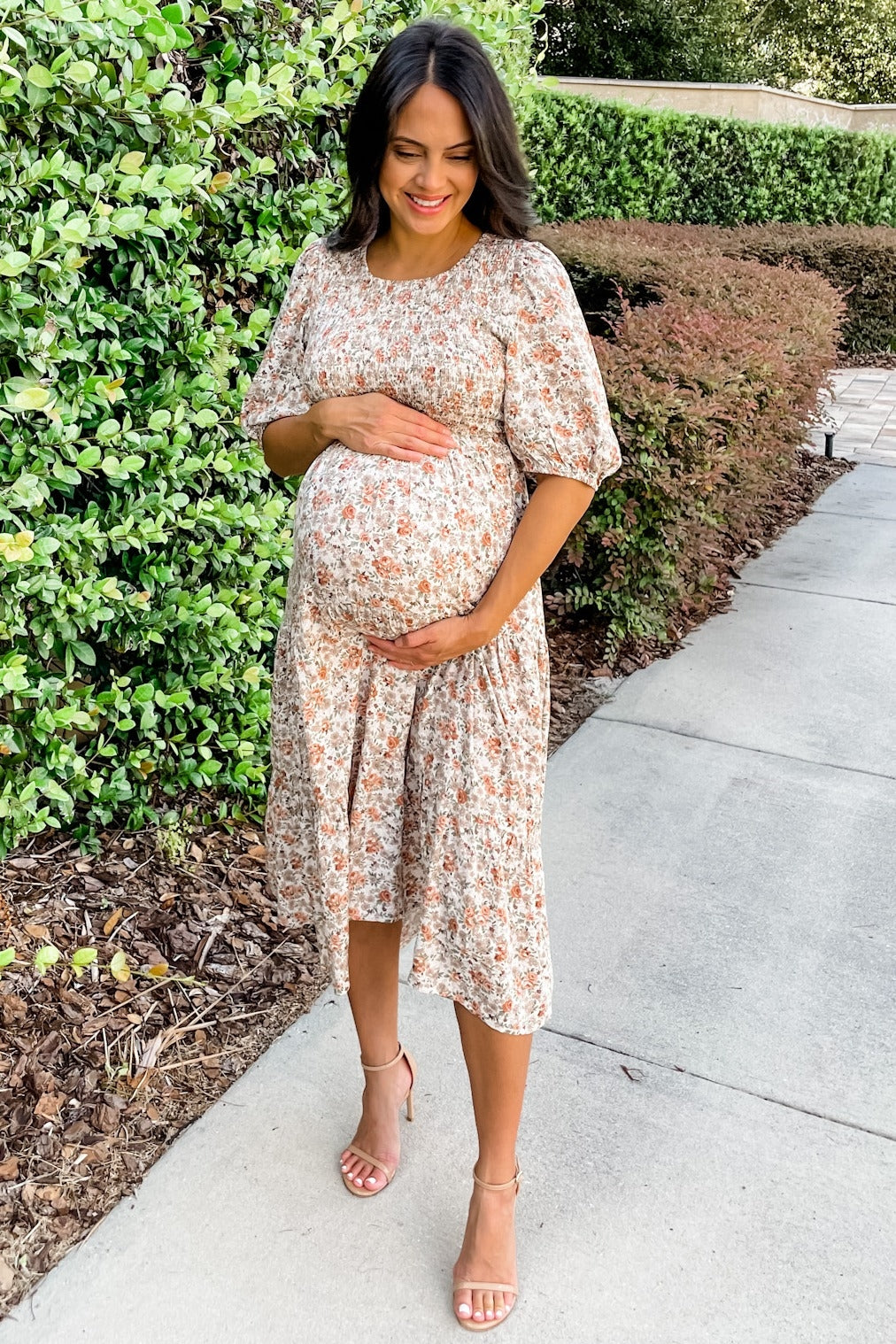 woman wearing a floral maternity dress and holding her baby bump while standing outdoors