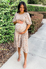 woman wearing a floral maternity dress and holding her baby bump while standing outdoors
