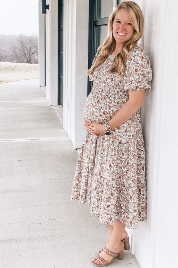 woman wearing a floral maternity dress and holding her baby bump while standing outdoors