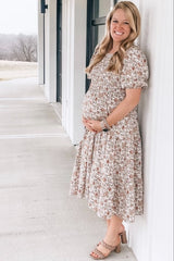 woman wearing a floral maternity dress and holding her baby bump while standing outdoors