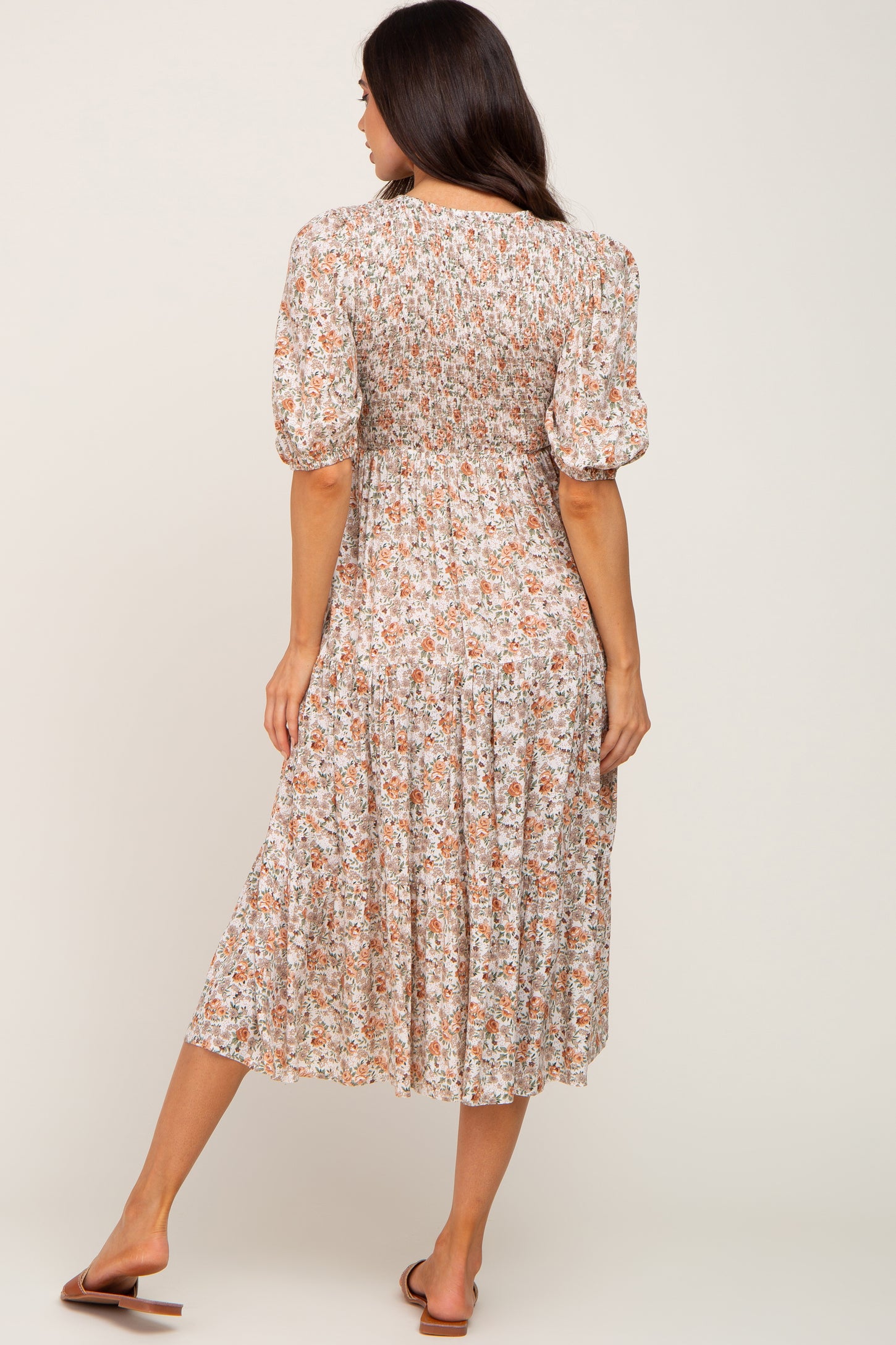 woman wearing a floral maternity mid-length dress with smocked bodice and puff sleeves, showing her baby bump from the back