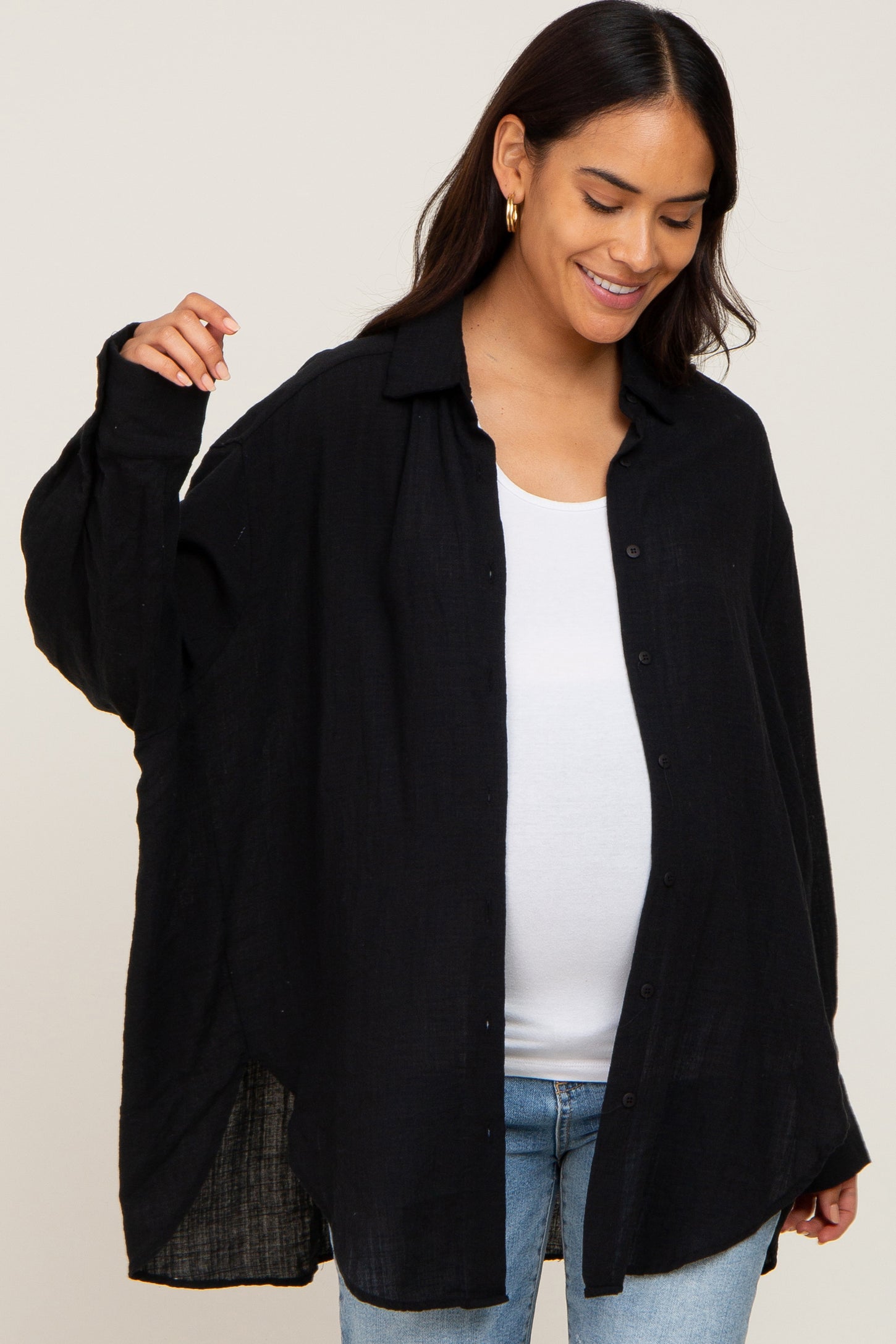 woman wearing a black oversized maternity shirt with a button-up front and a white tank top, showing her baby bump