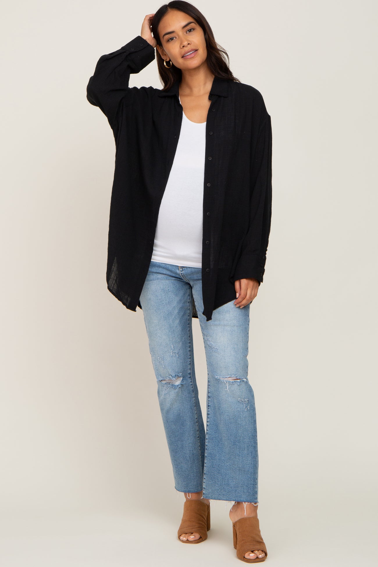 woman wearing a black oversized button-up shirt and light blue distressed flared jeans, showing a baby bump