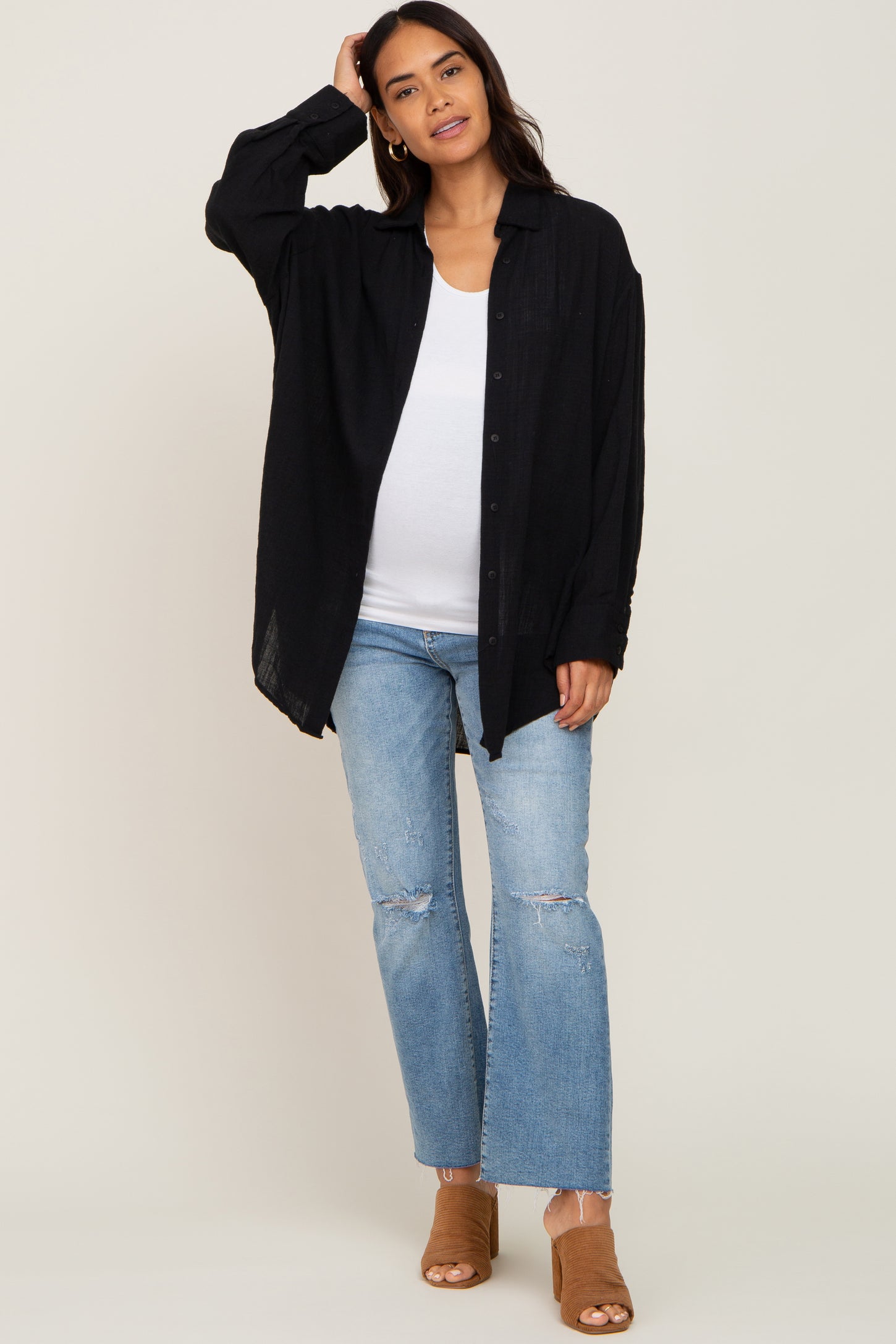 woman wearing a black oversized button-up shirt and light blue distressed flared jeans, showing a baby bump