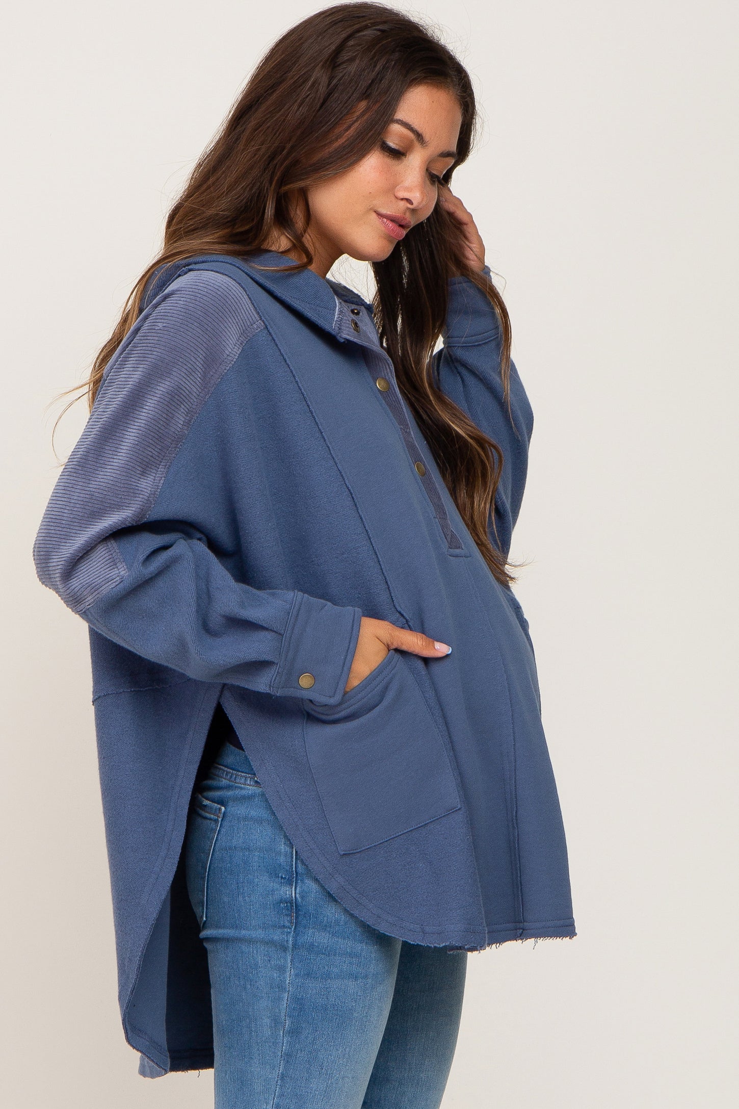 woman wearing a blue maternity pullover with a hood, front buttons, and pockets, lightly distressed hem, and a visible baby bump