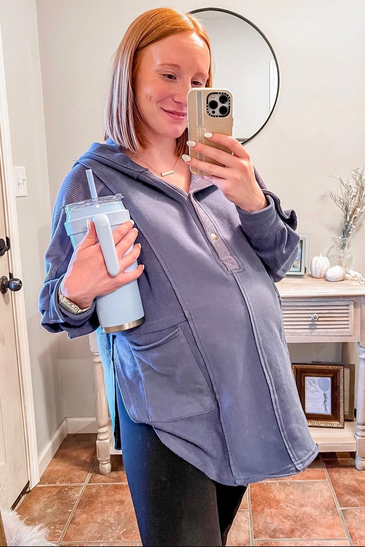 woman wearing a navy blue maternity hoodie, showing baby bump, holding a light blue tumbler in her other hand