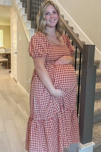 woman wearing a red and white checkered maternity dress, holding her baby bump, standing on staircase