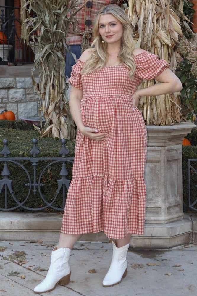 woman wearing a red and white gingham off-the-shoulder maternity dress and holding her baby bump, paired with white cowboy boots