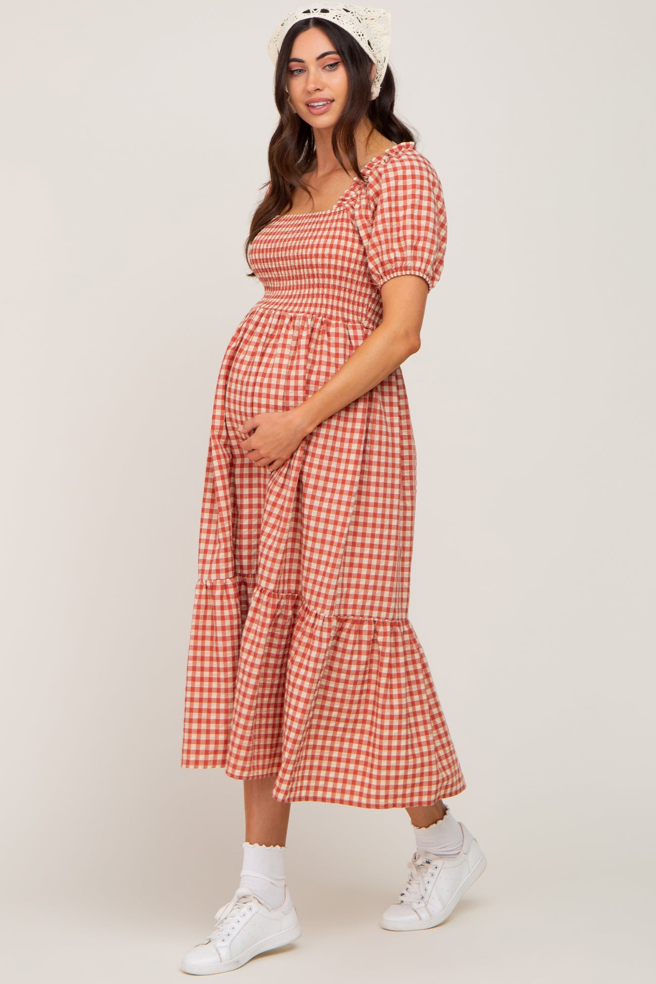 woman wearing a red and white checked maternity dress with short puff sleeves and a tiered skirt, showing her baby bump