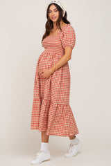 woman wearing a red and white checked maternity dress with short puff sleeves and a tiered skirt, showing her baby bump